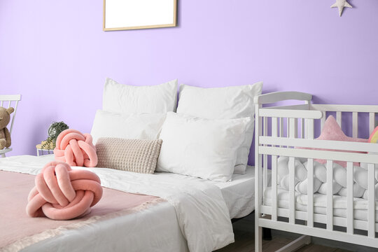 Baby Crib And Comfortable Bed Near Violet Wall In Stylish Room