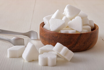 Bridge-shaped sugar cubes in wooden bowl on white wooden background. Low angle closeup view, no people.