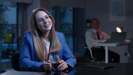 Attractive young businesswoman drink coffee and look at screen sitting at desk in modern office