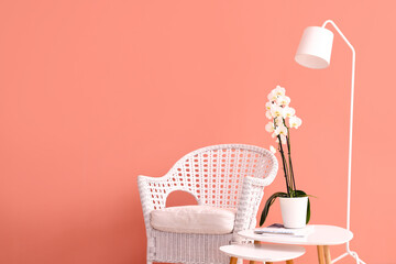 Wicker chair, table with orchid flower and floor lamp near color wall