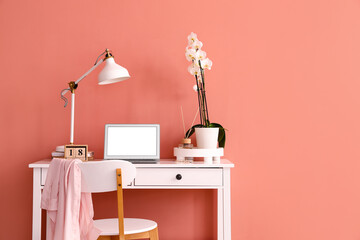 Stylish workplace with modern laptop and orchid flower near color wall