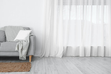 Grey sofa with pillow and plaid near light wall