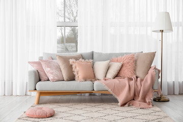 Grey sofa with cozy pillows, plaid and lamp near window