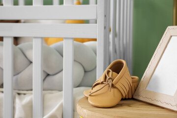 Table with baby booties and frame near crib, closeup