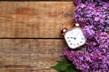 Purple lilac flowers with alarm clock on wooden background