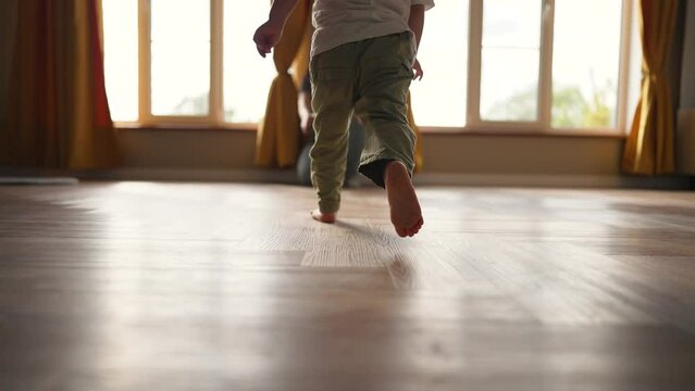 Happy family. Baby feet walk on floor towards mother. Child makes steps barefoot on parquet floor in children room. Son runs to his mother on the laminate with his bare feet. happy baby first steps