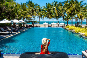 Luxury beach vacation in tropical beach hotel. Tourist woman in red dress relax near blue swimming...