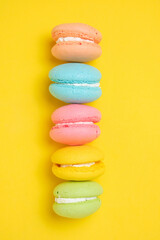 Colorful and bright French macarons cookies on yellow background.