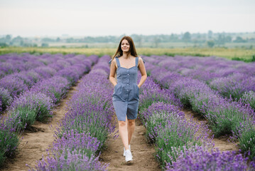 Girl walking in a lavender flowers field. A beautiful woman walk on the lavender field. Enjoy the floral glade, summer nature. Natural cosmetics concept.