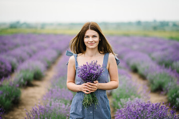 Beautiful girl in a dress in purple lavender field. Woman walking on the lavender field. Female collects lavender. Enjoy the floral glade, and summer nature. Natural cosmetics and eco makeup concept.