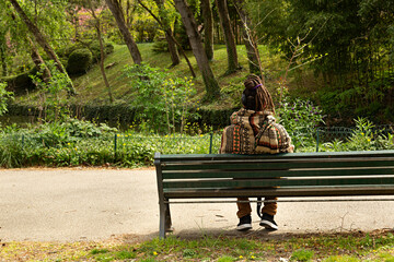Hombre joven sentado en banco de un parque oyendo música.