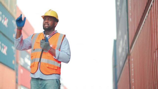 African American cargo container worker as foreman or technician use walkie talkie to comunicate with his co-worker in workplace in day time.