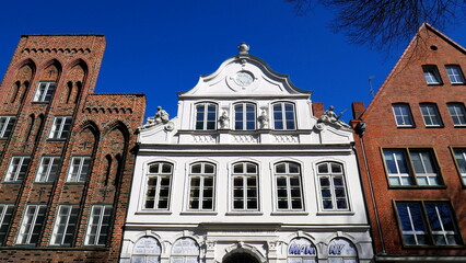 weißes Buddenbrooks Haus in Lübeck umrahmt von alten roten Backsteinfassaden unter blauem Himmel