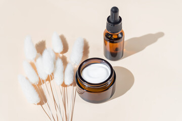 Face oil and cream moisturizer on light beige background with dry flowers. Set of cosmetic beauty products with natural extracts. Daily skincare routine.