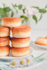 Many delicious golden donuts on a table with mint and daisy.