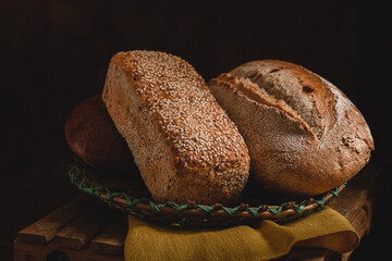 Whole grain breads in a wicker basket. Sesame bread and rye bread on a dark rustic background.