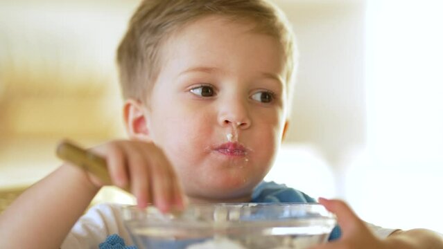 baby eats cereal porridge.Child sits at table and eats porridge.Family breakfast in kitchen.Child at table in kindergarten.Child proper nutrition.Breakfast in kindergarten.Happy dirty child with spoon