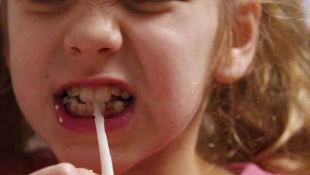 Close-up of a cute child girl with big blue eyes gnawing on a squid with her teeth. The girl's mouth is stained with sesame seeds. Selective focus