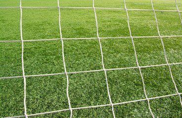 The soccer green field viewed through white square gate net. Football sport background. close-up, soft focus. Focus on a grass.