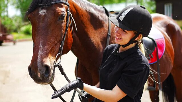 Lovely young woman wearing helmet stroking to her brown horse