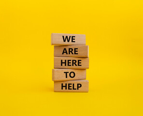 We are here to help symbol. Concept words we are here to help on wooden blocks. Beautiful yellow background. Business and we are here to help concept. Copy space.