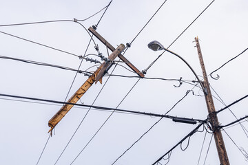 Low angle view of a severed wooden utility pole, tangled with overhead electric supply wires in the...