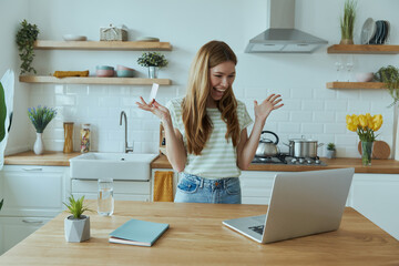 Excited young woman enjoying online shopping and using credit card while sitting at the kitchen