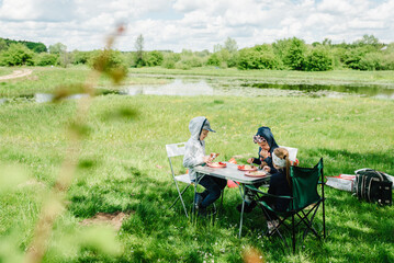Children sit at the table and smile at the picnic. Kids eat and having picnics near lake on the...