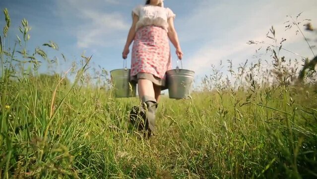 Close-up of a milkmaid carrying buckets and walking through tall grass
