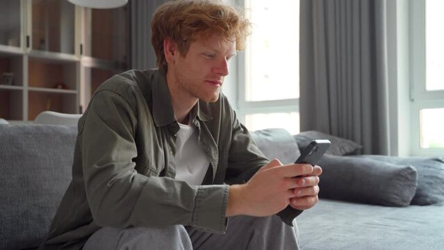 Smiling young adult ginger irish freelance business man using mobile phone