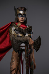 Shot of female viking warrior with axe and tattooed body isolated on grey background.