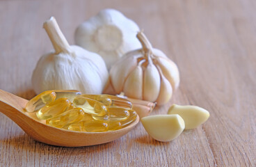 Garlic oil in capsules, gel, in a wooden spoon. as a health healthy vitamin supplement
