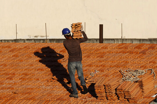 Roofer working on roofing construction. Bricklayer roof repair. House under construction. Workman renovates waterproofing roof of building. Carpenter construction worker carry pile of tiles