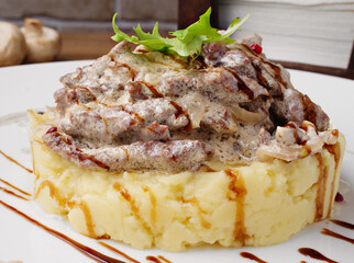 Beef Stroganoff with mashed potatoes on a white plate on a wooden background. Serving dishes in the restaurant. Lunch, dinner. Photos for the menu. Mashed potatoes and meat with mushrooms. Copy space.