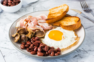 English breakfast with fried egg, bacon, beans, mushrooms and toast on a plate on the table.  Close-up