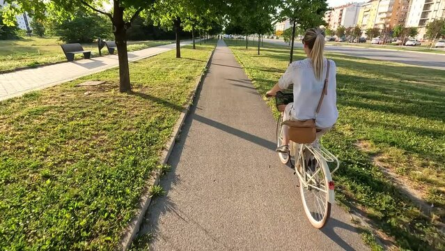 Rear view of young woman rides a bike on city street, slow motion 4k