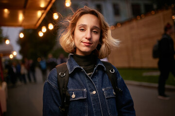 evening portrait of a beautiful young girl dressed in a denim jacket with a backpack. girl dressed...