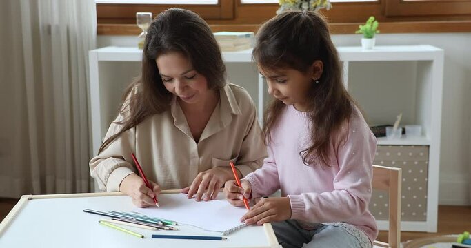 Loving mom and daughter drawing together with colored pencils, engaged in creative hobby painting pictures in paper sketchbook look happy enjoy pastime in nursery. Leisure, kids development concept