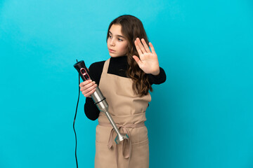 Little girl using hand blender isolated on blue background making stop gesture and disappointed