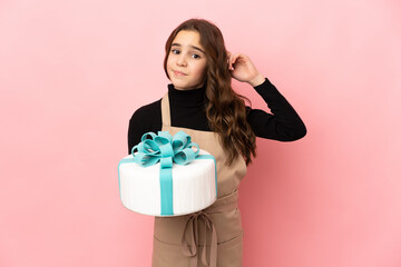 Little Pastry chef holding a big cake isolated on pink background having doubts