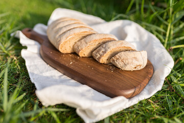 Composition of homemade white flour bread on wood board with white cloth napkin on the green grass . High quality photo