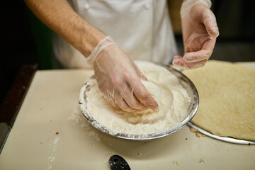 cook in gloves knead pizza dough. hands of pizza maker knead the dough for pizza with flour on a...
