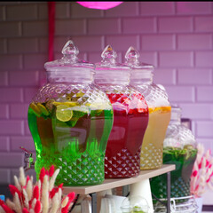 Large glass jars with soft drinks of green red and yellow color are on the counter