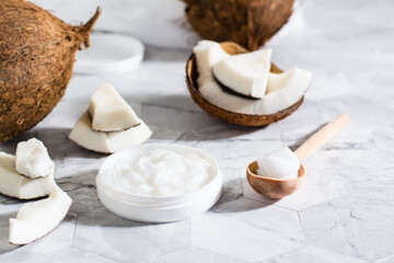 Fototapeta na wymiar Fresh coconut oil in a jar and spoon and pieces of coconut on the table. Natural cosmetic
