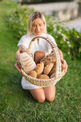 Young woman in white dress sitting on the grass with basket with assorti of brown and white homemade bread. High quality photo
