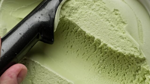 Flavored pistachio ice cream scooping out of container by spoon. Top view of surface of green ice cream. Delicious dessert. Close-up in 4K, UHD