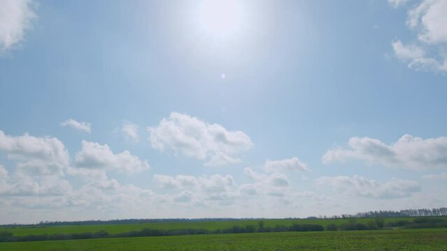 White clouds move across the blue sky over fields. Countryside outdoors, relaxation weather.