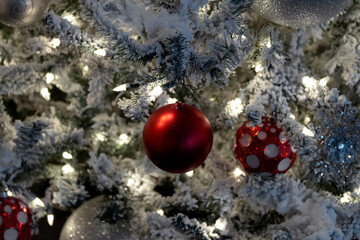 close up christmas decoration scene, white lights on snow covered tree with red and white christmas balls, festive holiday scene