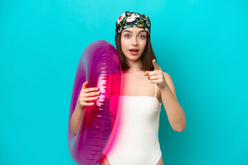 Young Ukrainian woman holding air mattress isolated on blue background surprised and pointing front