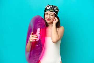 Young Ukrainian woman holding air mattress isolated on blue background frustrated and covering ears